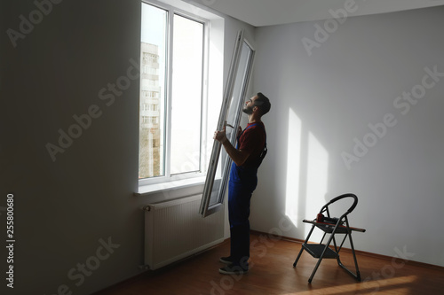 Construction worker installing plastic window in house