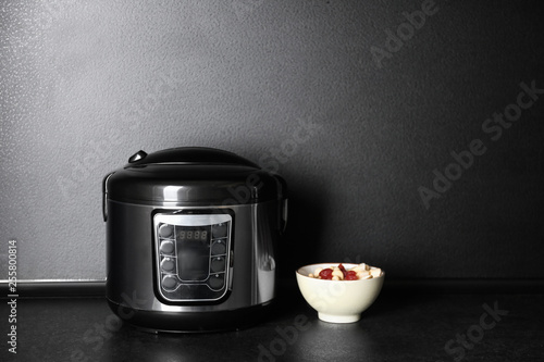 Modern multi cooker and ingredients on table near dark wall, space for text