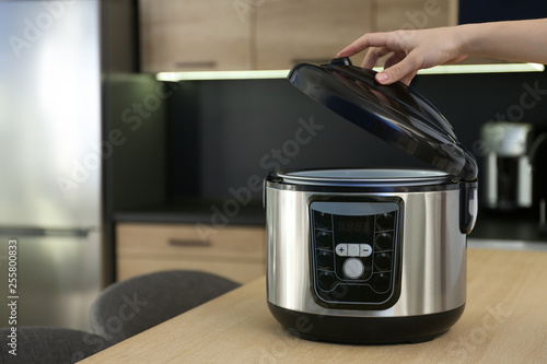 Young woman using modern multi cooker in kitchen, space for text