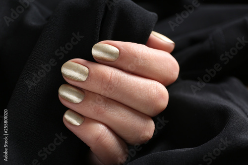 Woman with golden manicure holding black fabric, closeup. Nail polish trends