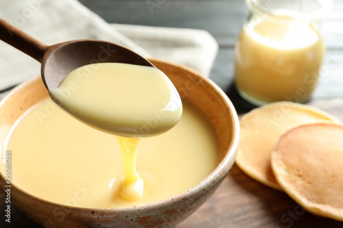 Spoon of pouring condensed milk over bowl on table  closeup with space for text. Dairy products