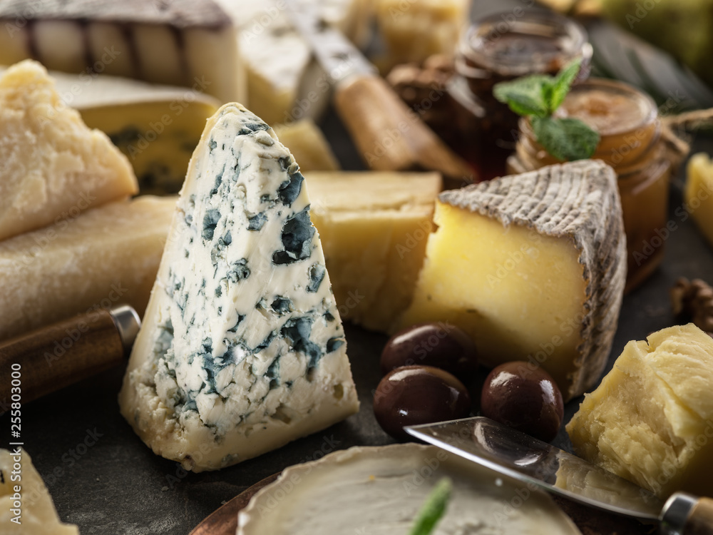 Segment of blue mould cheese with olives and range of cheeses at the background.