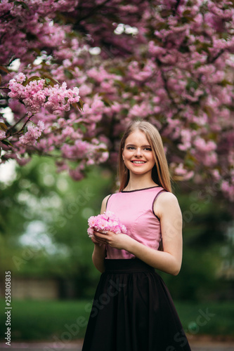 Portrait of European female near the Japanese flowering tree of sakura. Blond hair girl outside