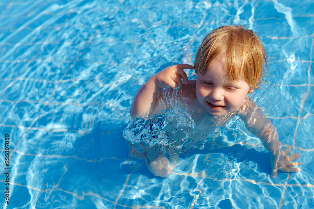 Happy little fair child boy in water in swimming pool