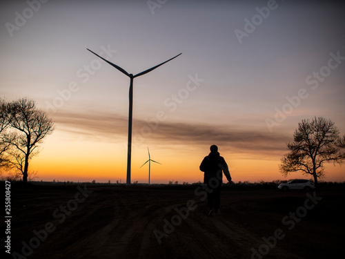 silhouette of a man goes to sunset in the direction of wind turbines