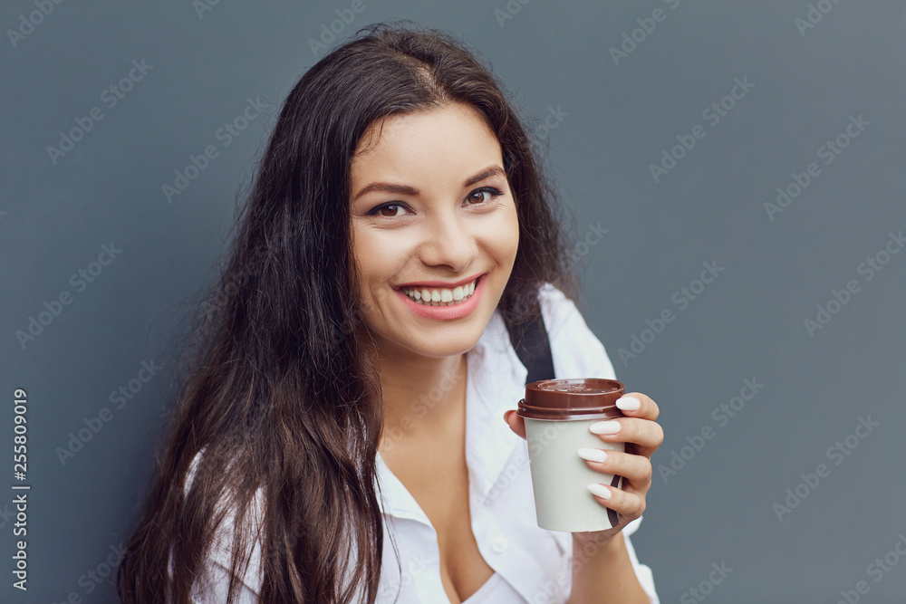 A brunette girl with a coffee mug at the gray background. A brunette girl with a coffee mug at the gray background.