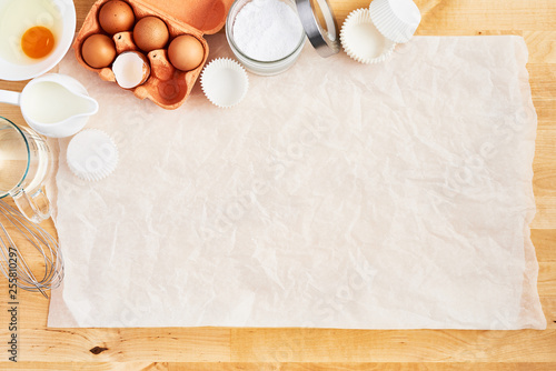 Food ingredients and kitchen utensils on crumpled piece of white parchment or baking paper on wooden table. Baking background concept. Top view. Copy space for text and design. photo