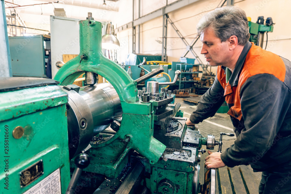 Turner worker manages the metalworking process of mechanical cutting on a lathe.