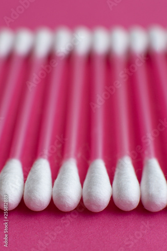 Closeup side view on cotton buds laid in a horizontal line on pink background