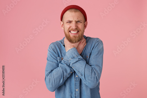Bearded man squeezes constrict with his hands the neck, especially so as to cause death, closed eyes, makes a suicide gesture, strangles himself, over pink background