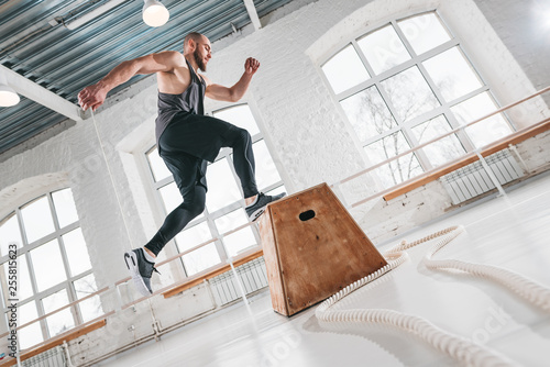 Strong man doing a box jump exercise at workout gym. Male athlete using box for crossfit exercises photo