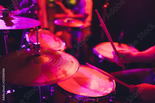 Leinwand Poster man plays musical percussion instrument with sticks closeup on a black background, a musical concept with the working drum, beautiful lighting on the stage