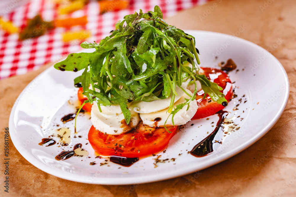 Caprese salad with arugula on white plate. Close up Caprese salad with arugula on white plate. Close up
