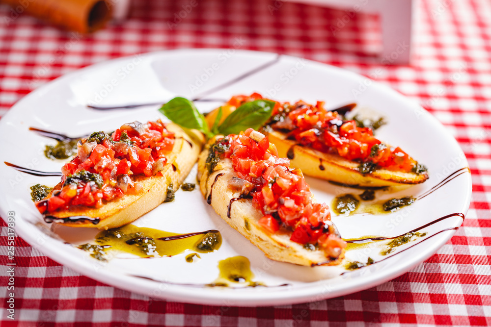 Traditional Italian bruschetta with cherry tomatoes, pesto sauce and balsamic vinegar on white plate. Close up Traditional Italian bruschetta with cherry tomatoes, pesto sauce and balsamic vinegar on white plate. Close up