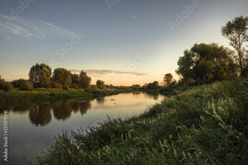 Narrow river summer scenery landscape with tranquil water mirror at sunset with clear sky and reflections riverbank 