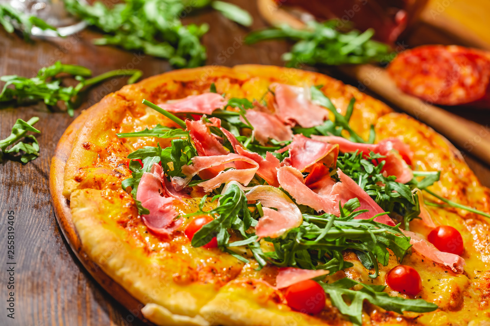 Italian pizza with prosciutto (parma ham), arugula (salad rocket) and cherry tomatoes on wooden board. Close up