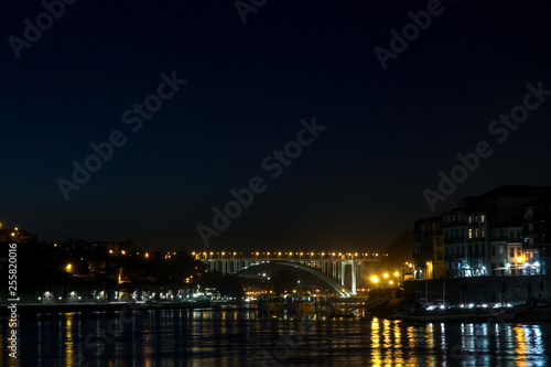 view of ponte da arrabida from gaia in porto, portugal at night with yellow light on bridge © c-foto