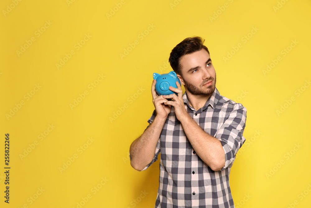 Young man with piggy bank on color background. Space for text Young man with piggy bank on color background. Space for text