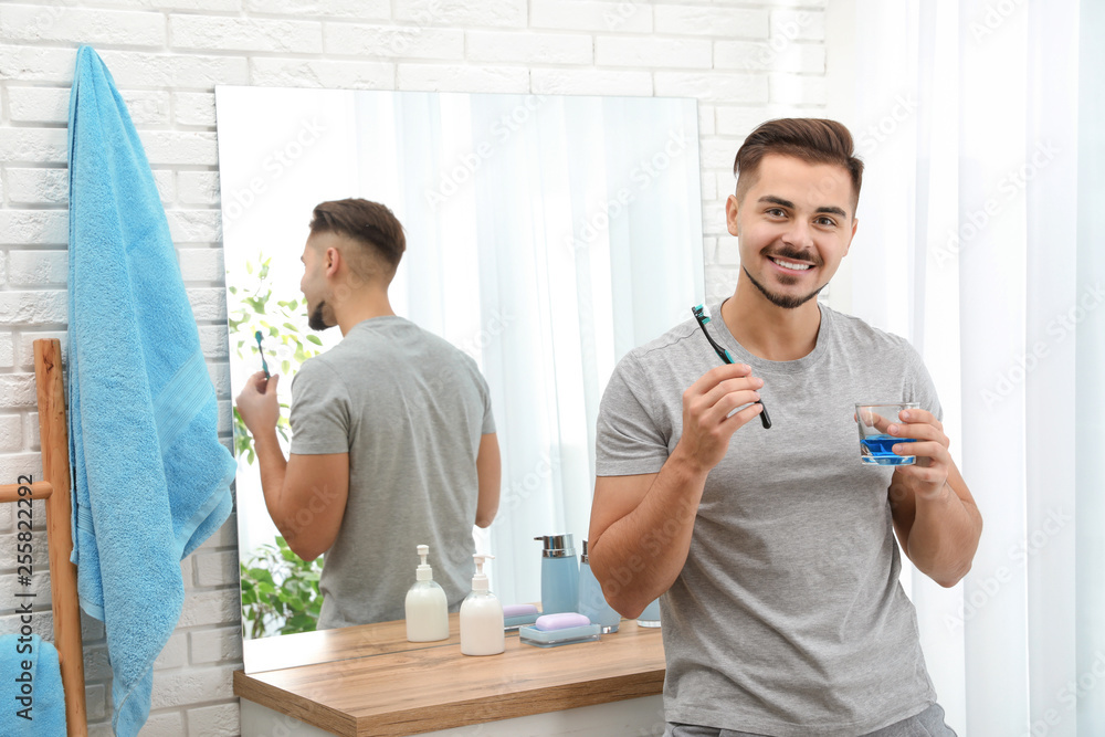 Obraz premium Young man with toothbrush and glass of mouthwash in bathroom at home, space for text. Teeth and oral care