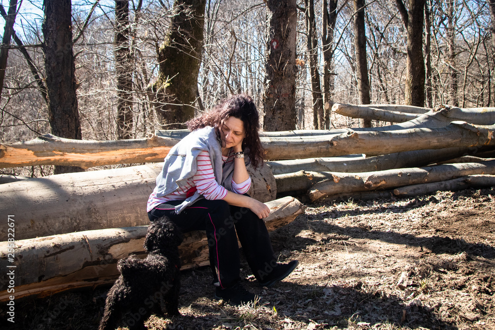 Woman sitting on trees in the forest with small poodle dog Woman sitting on trees in the forest with small poodle dog