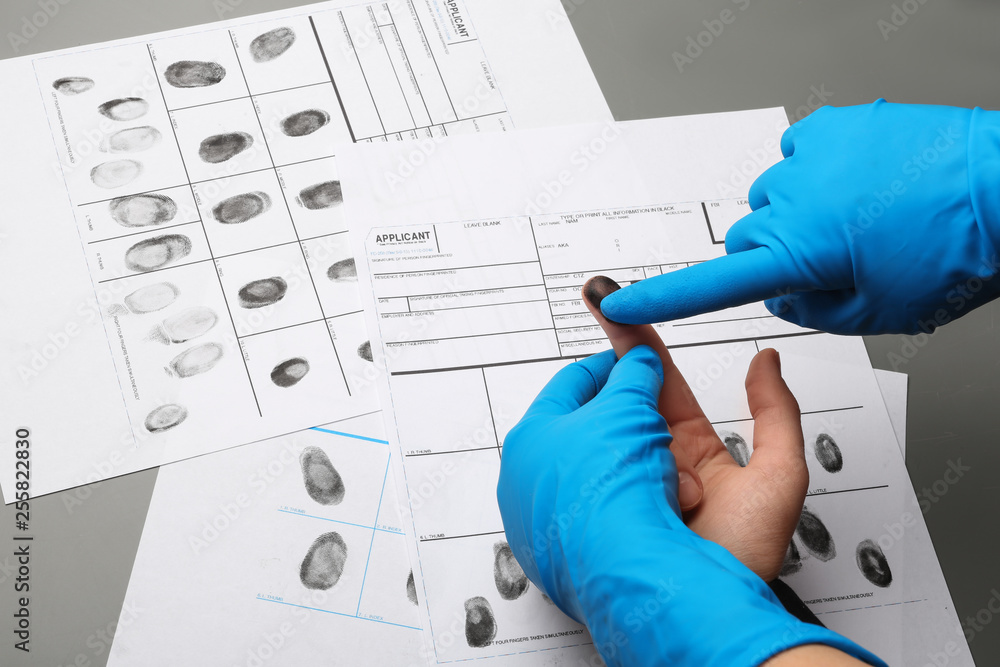 Investigator taking fingerprints of suspect at table, closeup. Criminal expertise Investigator taking fingerprints of suspect at table, closeup. Criminal expertise