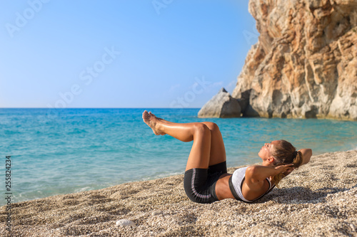 Beautiful young woman working out her abs on the beach
