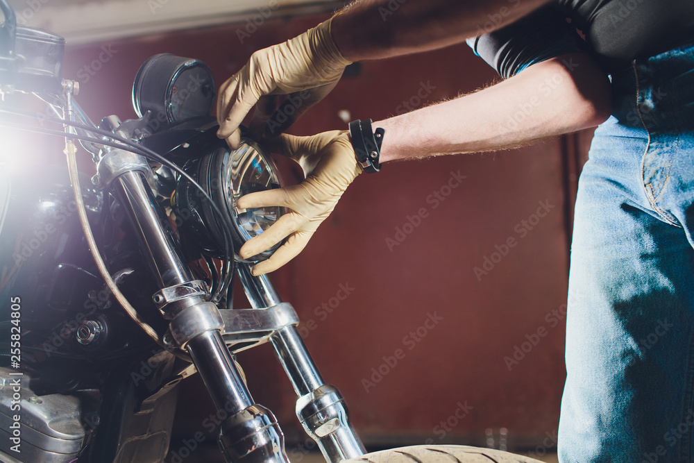 Fototapeta Man fixing bike. Confident young man repairing motorcycle near his garage. replacement lamp in the headlamp