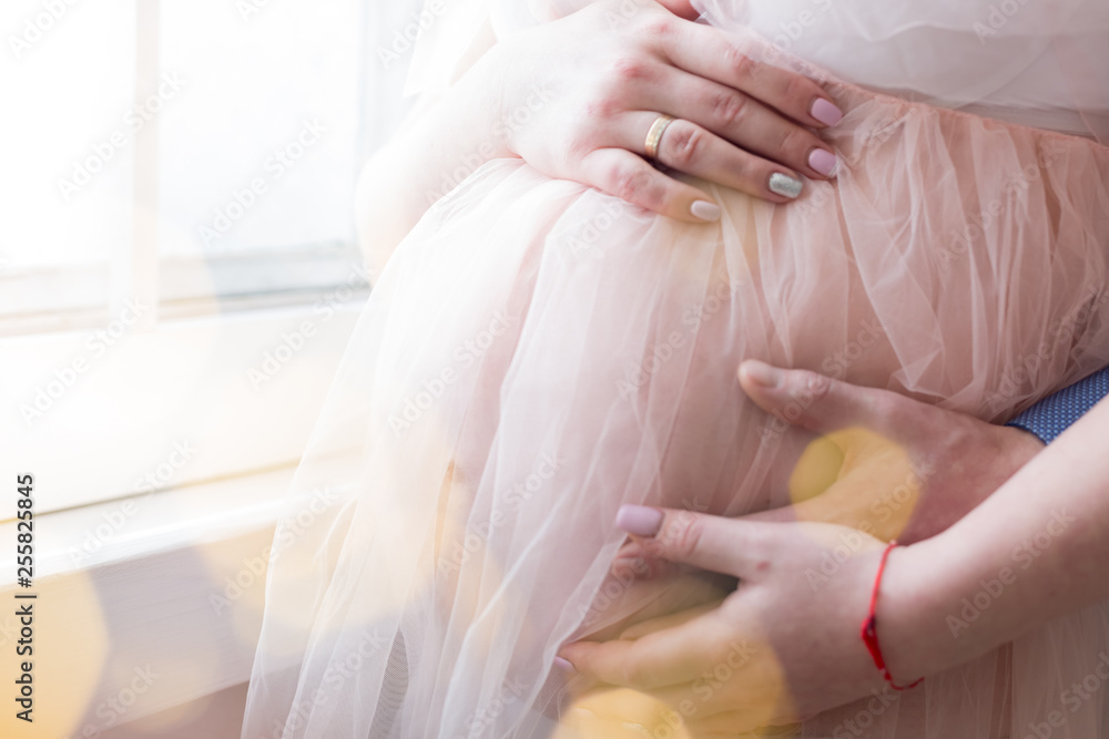 Fototapeta premium pregnant girl in peach-colored negligee. the hands of men and women in the abdomen. 