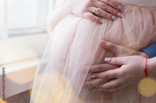 pregnant girl in peach-colored negligee. the hands of men and women in the abdomen. 