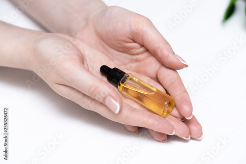 Yellow cuticle oil bottle and a female hands on a white wooden table background. Fingernail care concept.