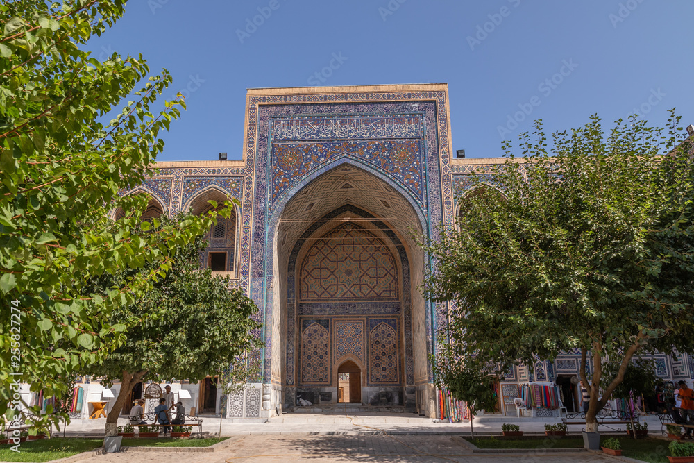 The Ulugh Beg madrasah view from the yard. In the courtyard of the Madrasah with trees. Inside the Madrasah on Registan square in Samarkand. Ancient Madrasah in Uzbekistan. Sunny summer day.
