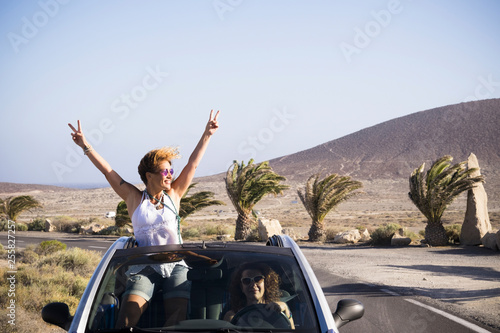 Couple of happy woman enjoy the trip traveling by car - driving and standing outside the roof with success and happiness pose - vacation in outdoor tropical place for cheerful people