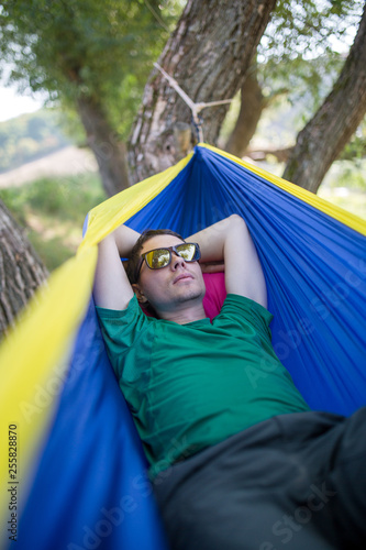 Photo of man in sunglasses lying in hammock in forest