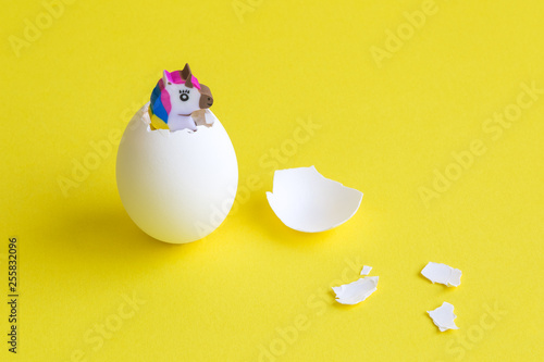 Unicorn hatching from egg against yellow background minimal easter creative concept.