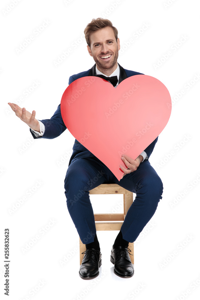 seated handsome man weolcoming with a red heart in hands seated handsome man weolcoming with a red heart in hands