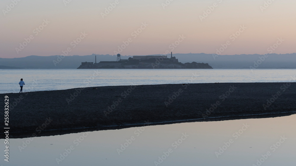 Lone jogger on the beach in San Francisco.  Alcatraz Island outlined against early morning sky.