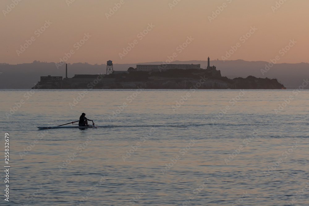 Solo rower in racing shell on calm water in front of Alcatraz.  