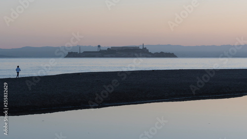 Lone jogger on the beach in San Francisco.  Alcatraz Island outlined against early morning sky. © colloidial