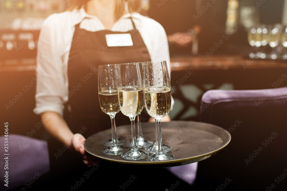 Full glasses of champagne on tray. Female waiter in uniform serving champagne.