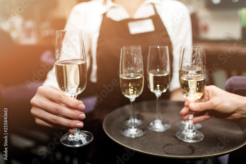 Full glasses of champagne on tray. Female waiter in uniform serving champagne.
