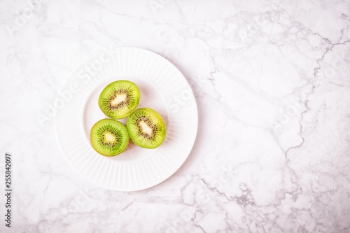 Three halves of ripe kiwies on a white gray marble background. Top view, copy space photo