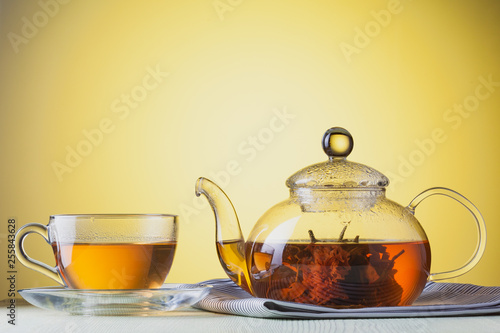 Transparent glass cup and teapot of flower green tea at yellow background