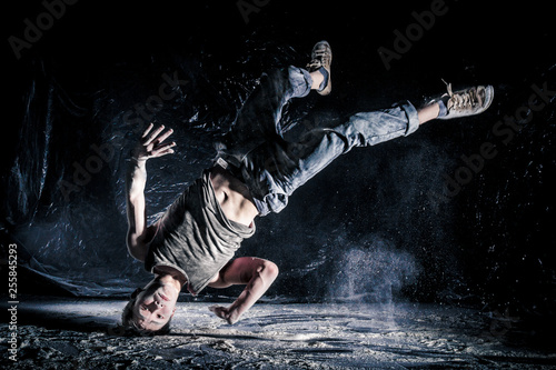 cool dirty vietnamese guy dancer in style of bboying doing complex tricks on floor in Studio filled with flour on black background. concept of space dance on surface of planet moon