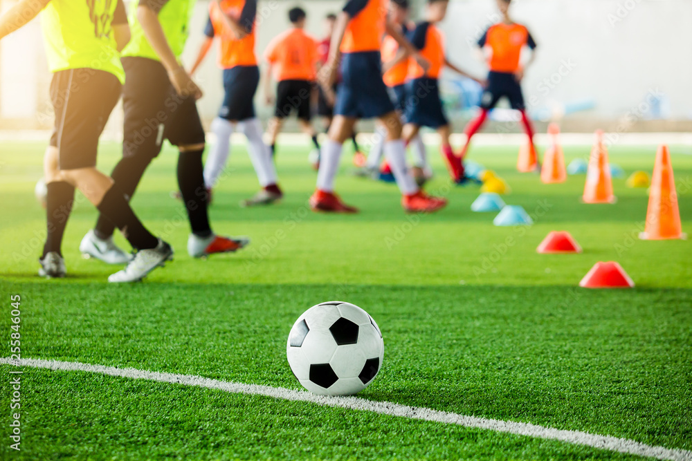 football on green artificial turf with blurry soccer team training, blurry kid soccer player jogging between marker cones and control ball with soccer equipment in soccer academy. football on green artificial turf with blurry soccer team training, blurry kid soccer player jogging between marker cones and control ball with soccer equipment in soccer academy.