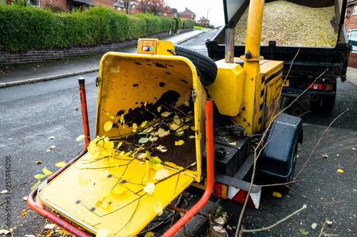 A yellow commercial engine powered drum woodchipper with hopper and wood chipper towed by a tipper truck photo