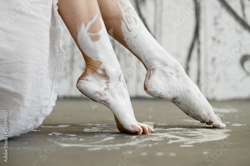 Legs and feet of a young artistically abstract painted woman, ballerina with white paint. Creative body art painting.