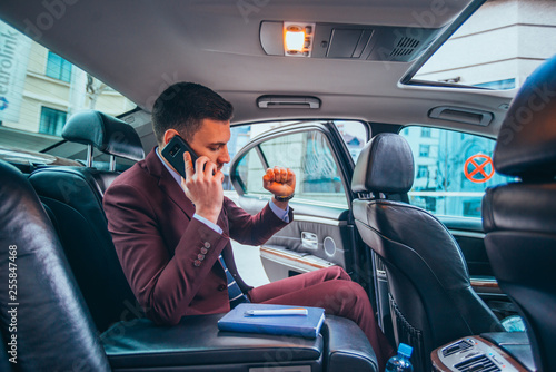 Businessman sitting in a limo while talking on his phone reading his notes and planning his day.