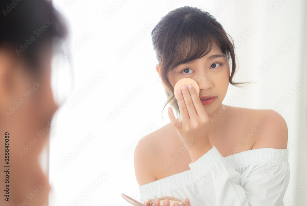 Portrait beautiful young asian woman applying powder puff at cheek makeup of cosmetic looking mirror, beauty of girl with skin face smile in the bedroom, health and wellness concept. Portrait beautiful young asian woman applying powder puff at cheek makeup of cosmetic looking mirror, beauty of girl with skin face smile in the bedroom, health and wellness concept.