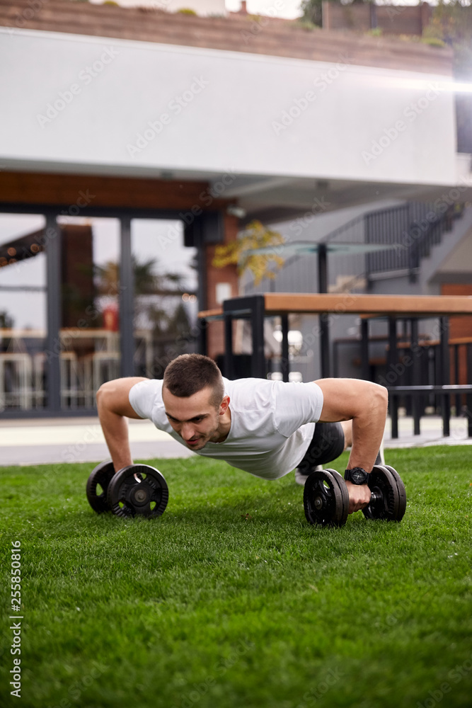 Fototapeta premium one young man,20-29 years old, doing push ups with weights in a beautiful backyard of a fancy house.
