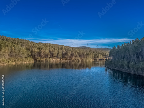 Aerial view of drone, forest with lake in mountain with wind turbines on ridge